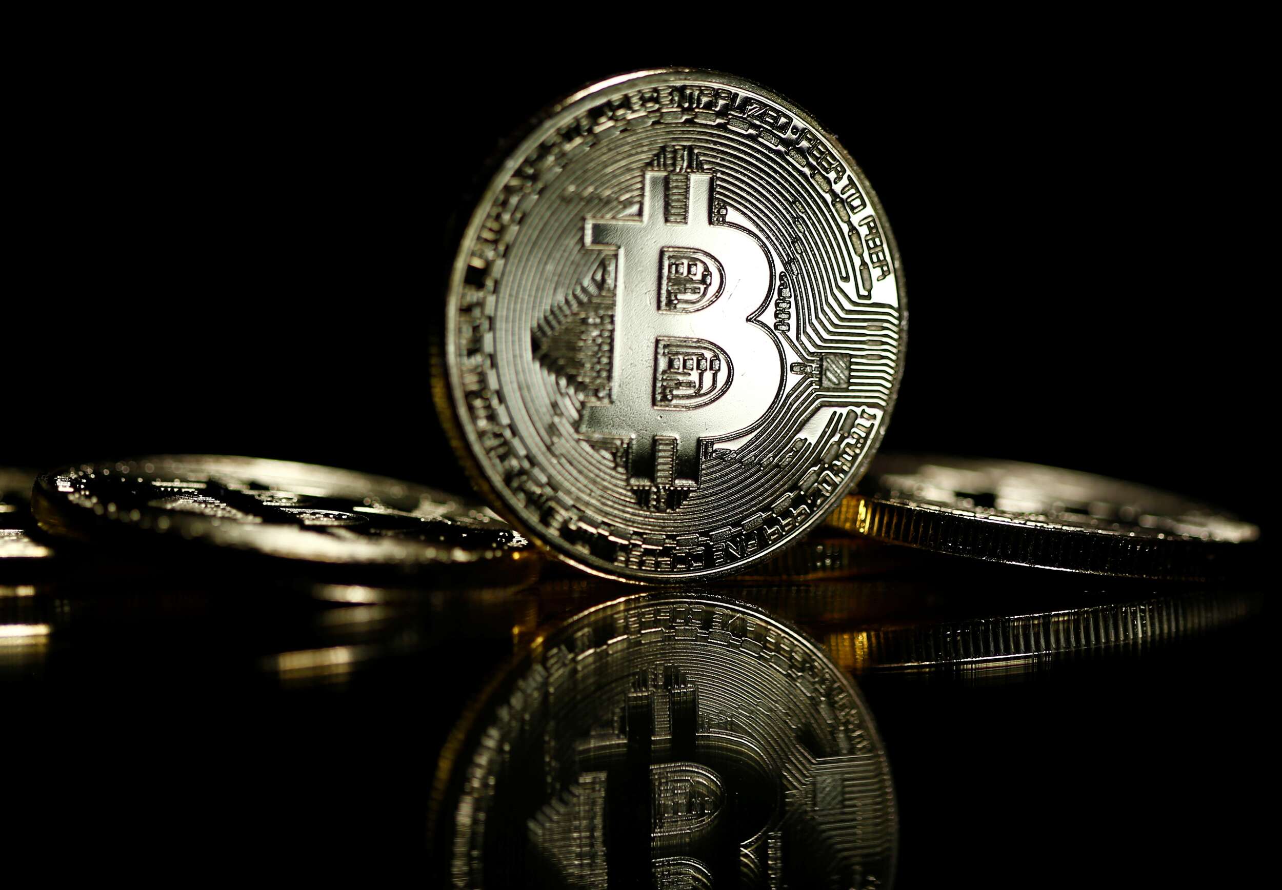 Picture of a standing bitcoin with two bitcoins lying on either side of it, with a black background