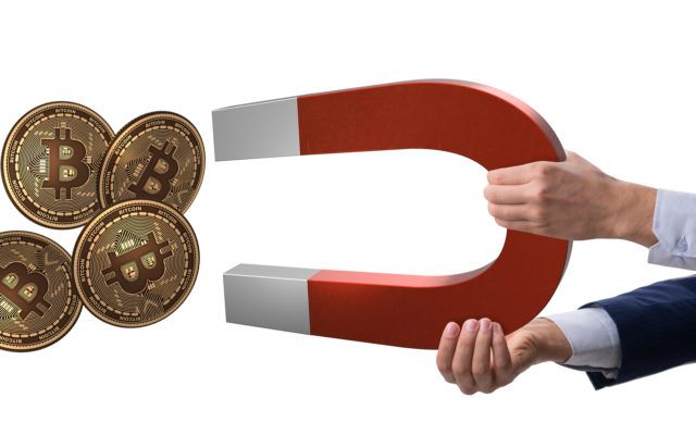 Picture of a hand attracting four gold bitcoin crypto coins with a giant red and white magnet